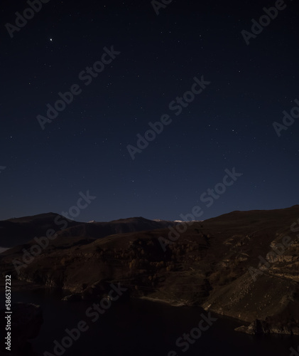 Night landscape in the mountains with rocky mountain ranges and night sky with stars, view from the cliff to the lake at night