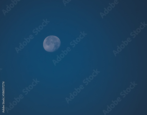 Minimalistic view of the waning moon against the blue sky, the moon is the satellite of the earth