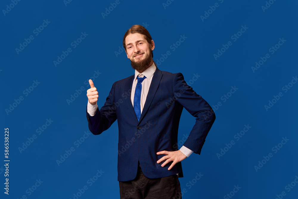 Approval. Portrait of happy young man in formal wear rising finger with pleasant gesture against blue studio background. Good job. Concept of emotions, facial expression, lifestyle, occupation Approval. Portrait of happy young man in formal wear rising finger with pleasant gesture against blue studio background. Good job. Concept of emotions, facial expression, lifestyle, occupation