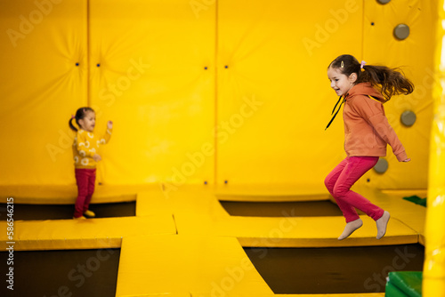 Siblings jumping on trampoline at yellow playground park. Sisters in motion during active entertaiments.
