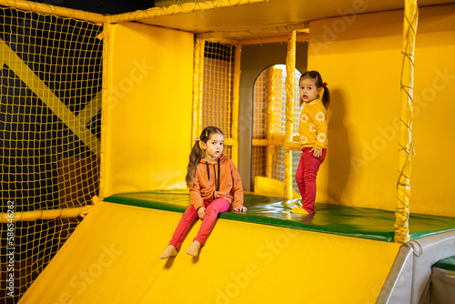 Siblings sliding at yellow playground park. Sisters in active entertaiments. photo