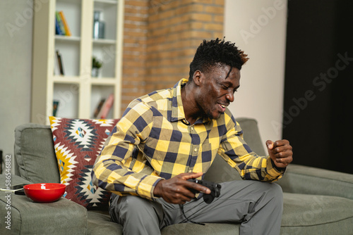 Young happy African guy playing video game at home. Man holding joystick and playing video games. photo