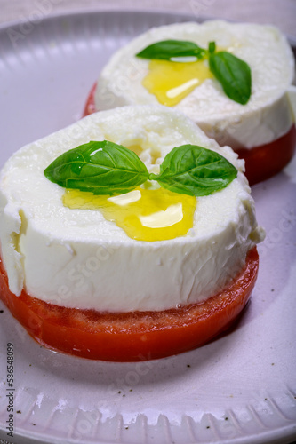 Sliced white ball of Italian soft cheese Mozzarella di Bufala Campana served with fresh green basil and red tomato