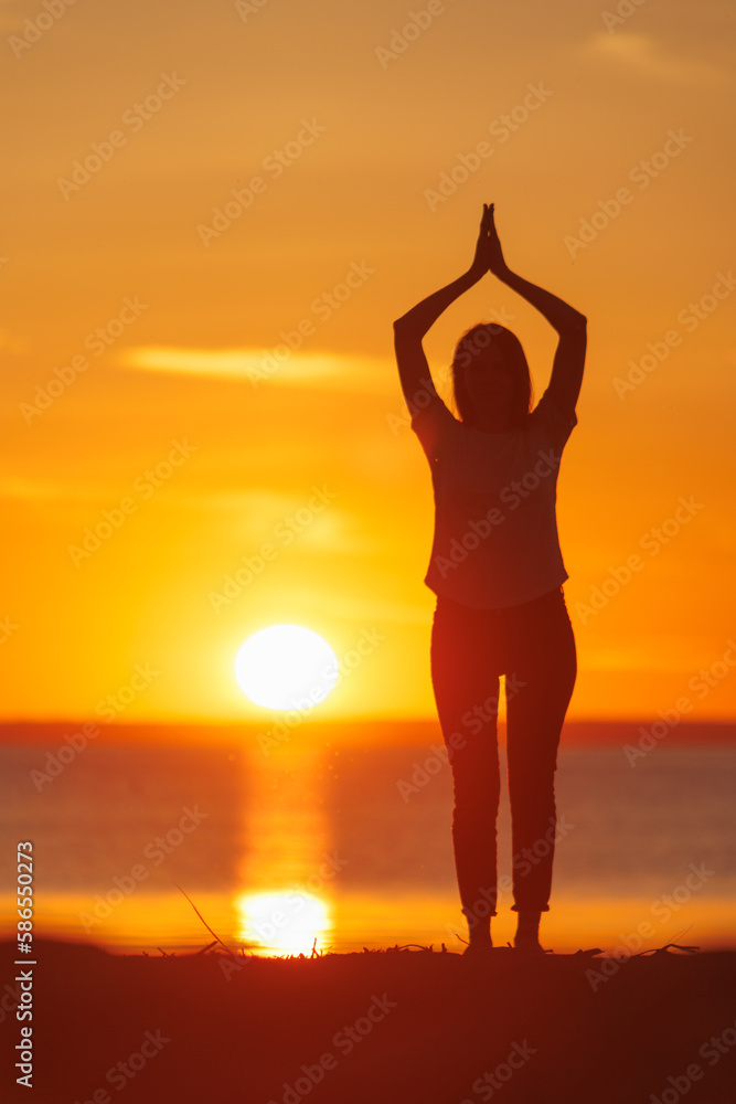 soft selective focus, yoga meditation, silhouette of woman at sunset in pose tree with outstretched arms. health recreation and outdoor sports. person is engaged in breathing practices. mental health