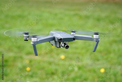 A flying quadrocopter against the background of grass in cloudy weather takes pictures of the surface of the earth.