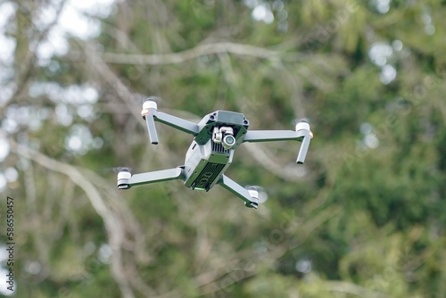 A flying quadrocopter against the background of trees in cloudy weather takes pictures of the surface of the earth.