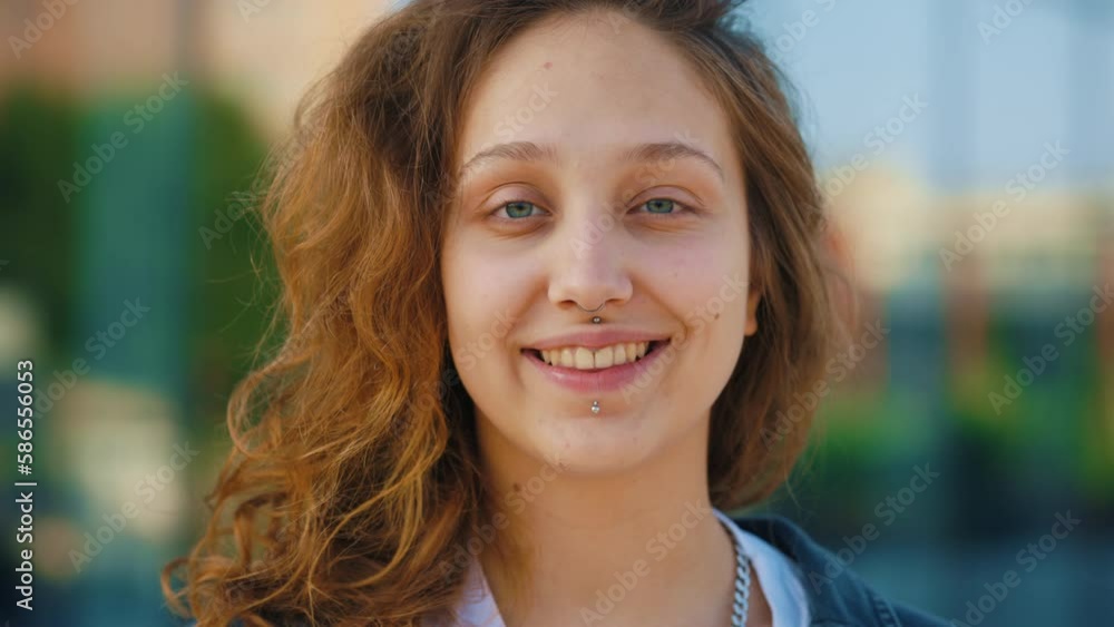 Portrait of the smiled beautiful girl with piercing looking at the camera standing outside, wearing casual clothes. Young cute lady looking straight to the camera. Close up. People concept. Portrait of the smiled beautiful girl with piercing looking at the camera standing outside, wearing casual clothes. Young cute lady looking straight to the camera. Close up. People concept.