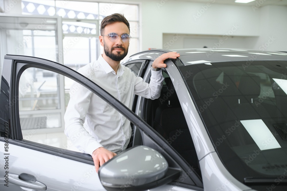 Happy young guy checking new luxury car, buying automobile at dealership centre. Portrait of cheerful millennial Caucasian man examining auto at showroom store Happy young guy checking new luxury car, buying automobile at dealership centre. Portrait of cheerful millennial Caucasian man examining auto at showroom store