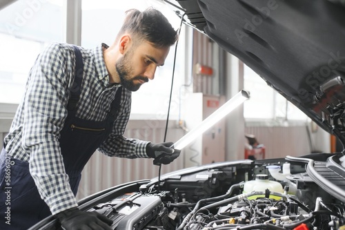 Professional Mechanic is Working on a Car in a Car Service. Repairman in Safety Glasses is Fixing the Engine on a Vehicle. Specialist Unscrews Bolts with a Ratchet. Modern Clean Workshop