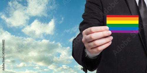  Businessman hand with a white banner on the background of LGBT flag. Equality, diversity, freedom concept