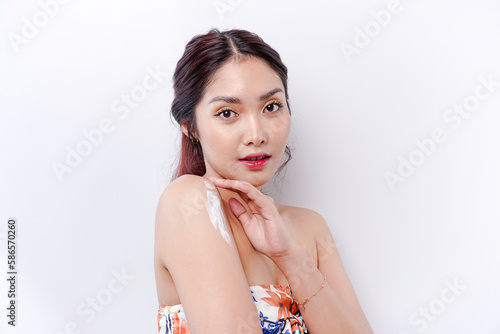 Skin Care Products Concept. Asian woman applying moisturizing lotion on body after shower  standing wrapped in towel  cropped image