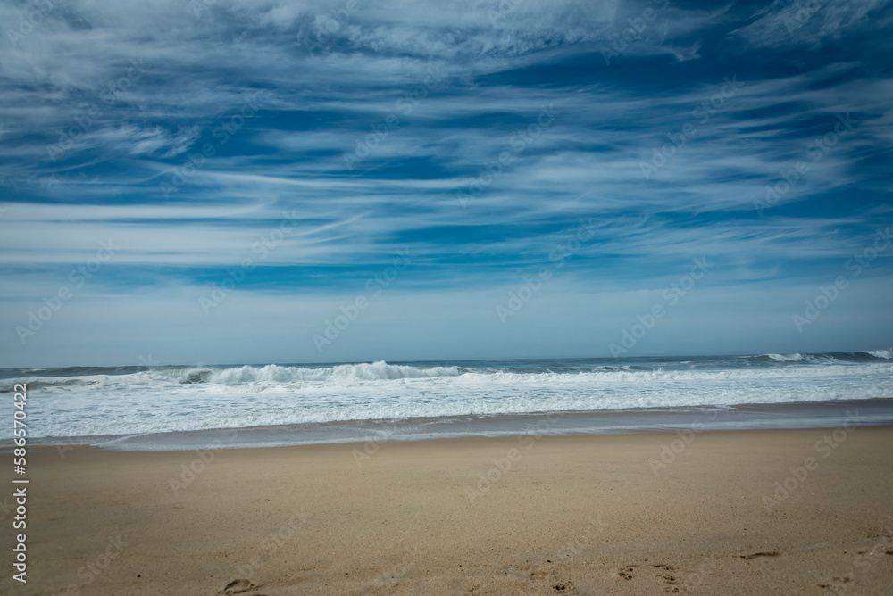 Symmetry between the sky and the beach. Blue sky covered by clouds, contrast with the foam of the waves. Espinho, Portugal