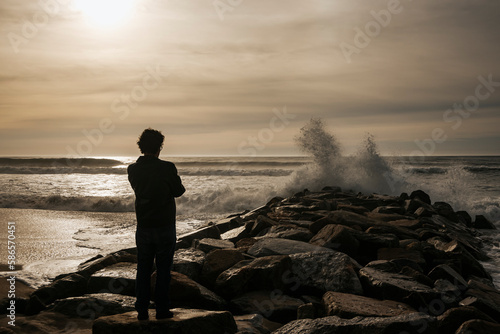 Man against cold sunset backlight. Waves crashing against the rocks on the beach. Espinho, Portugal