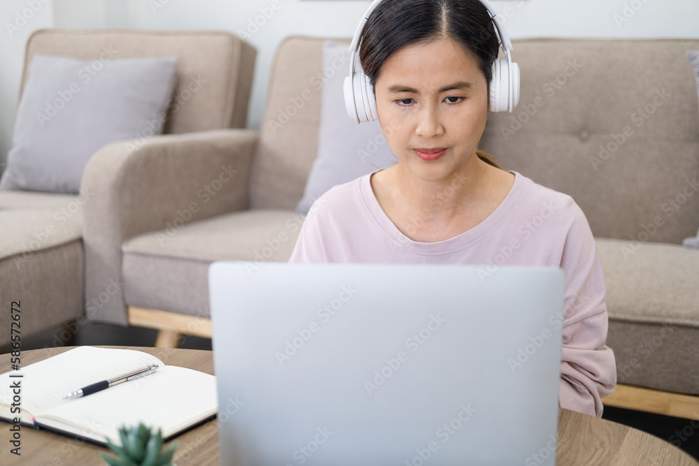 Focused woman wearing headphones using laptop in cafe, writing notes, attractive female student learning language, watching online webinar, listening audio course, e-learning education concept Focused woman wearing headphones using laptop in cafe, writing notes, attractive female student learning language, watching online webinar, listening audio course, e-learning education concept