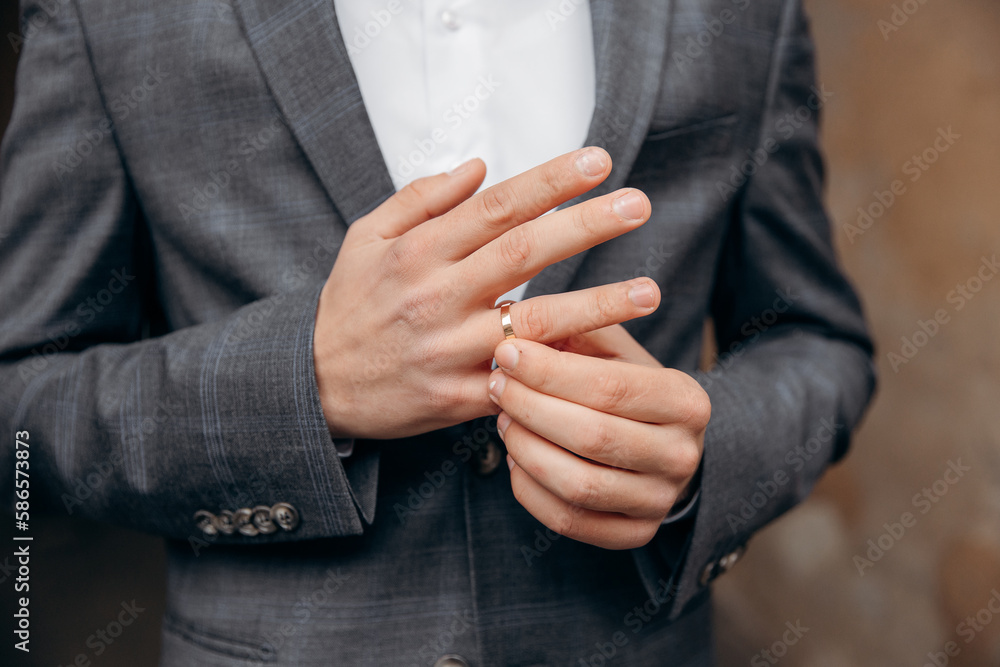 The groom in gray jacket and red bow-tie puts his wedding ring on his finger. Wedding ceremony. Close-up photo of a man's hands with a wedding ring