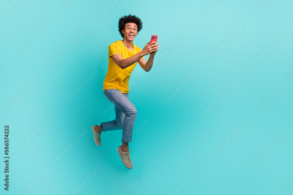 Full length photo of excited active man jumping rush use smart phone empty space isolated on teal color background Full length photo of excited active man jumping rush use smart phone empty space isolated on teal color background