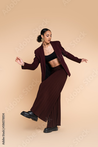 full length of african american woman in trendy maroon suit with wide leg pants posing on beige. © LIGHTFIELD STUDIOS