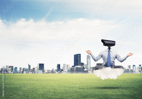 Camera headed man sitting in lotus pose on cloud against modern cityscape