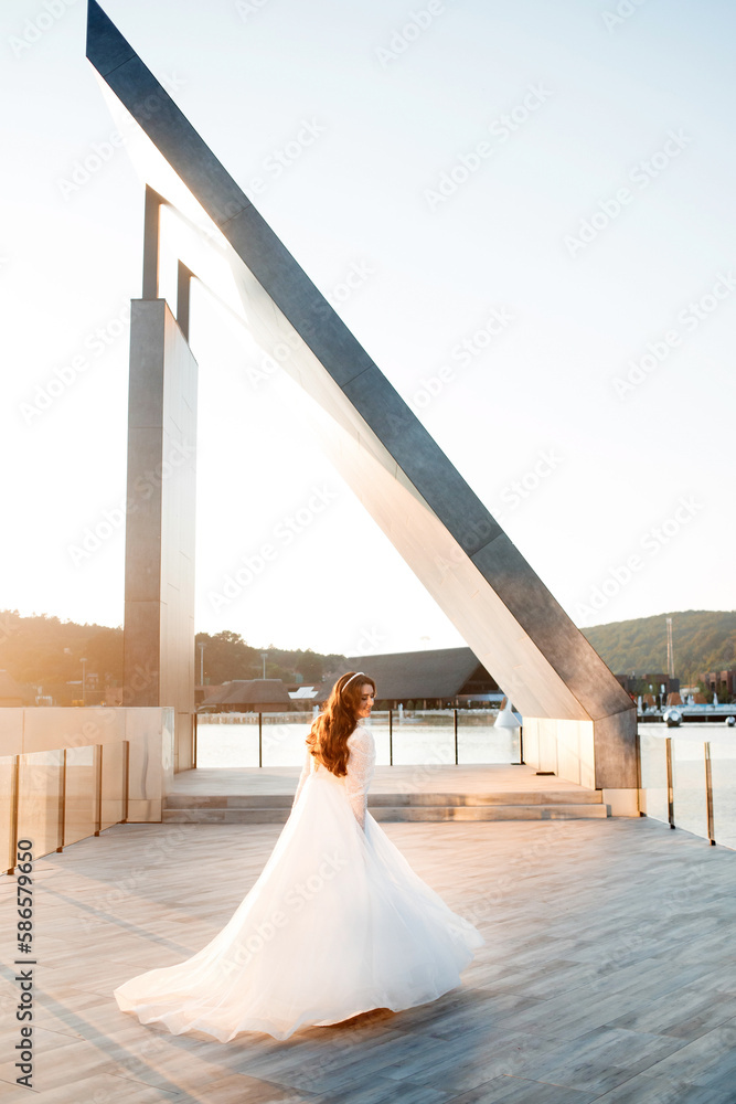 Obraz premium A beautiful bride in a long white dress against the background of the sunset