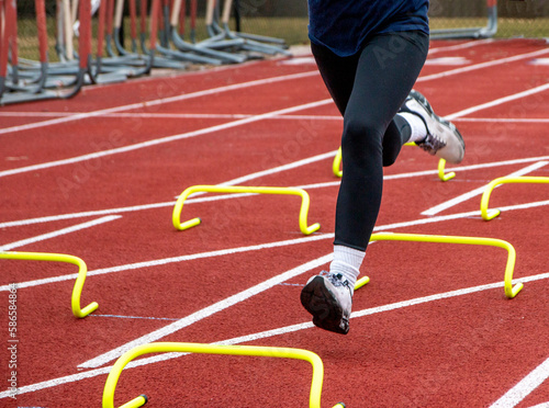 Legs of a runner running over six inch yellow hurdles on a track