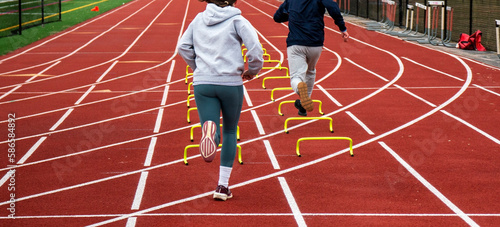 Two runners running over six iinch hurdles in lane on a track