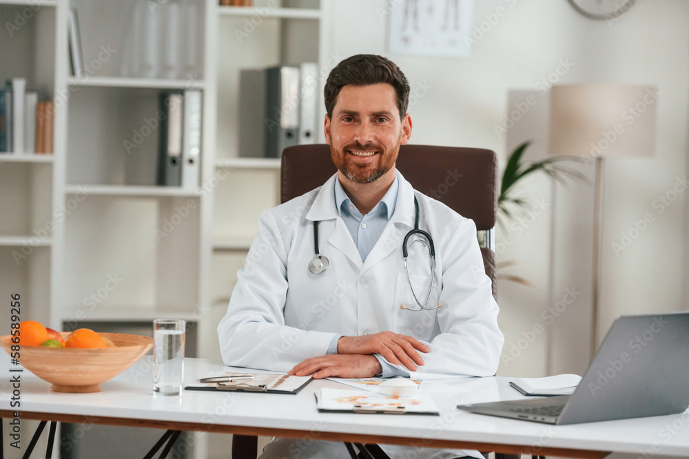 By the table with laptop. Doctor in formal clothes is working in the cabinet By the table with laptop. Doctor in formal clothes is working in the cabinet