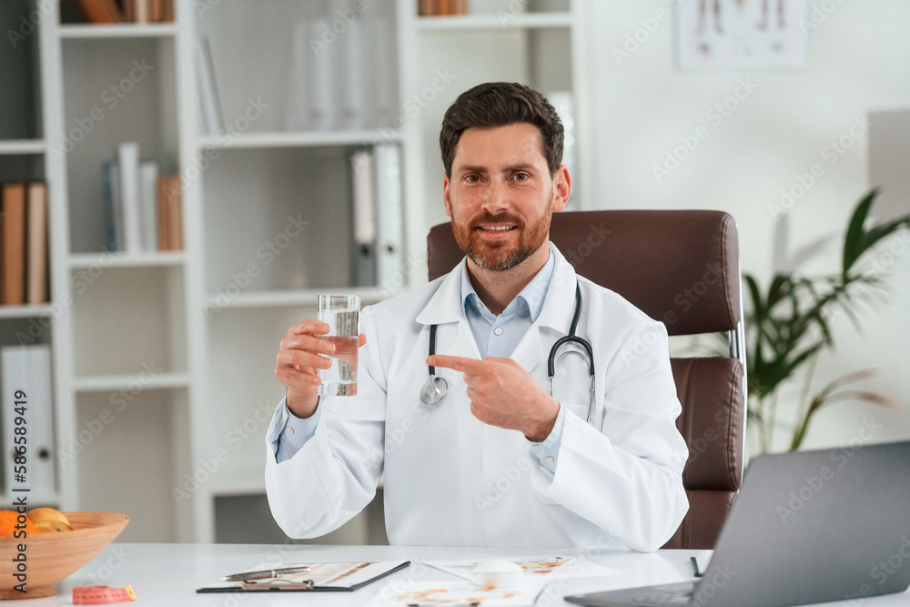 Holding glass with water. Doctor in formal clothes is working in the cabinet Holding glass with water. Doctor in formal clothes is working in the cabinet