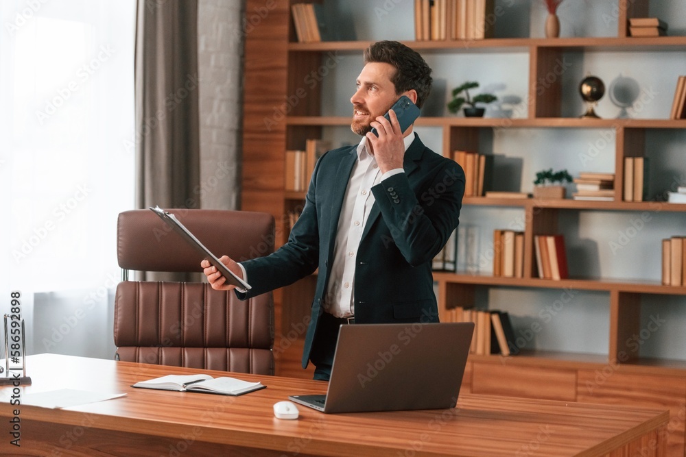 Talking by phone. Businessman in formal clothes is working indoors Talking by phone. Businessman in formal clothes is working indoors