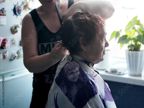 Woman hairdresser provides hair cutting service to elderly people at home. Caring for and caring for the elderly.
