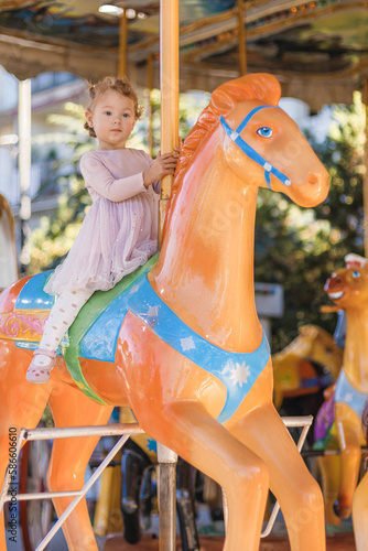 kid riding on a merry go round. Little girl playing on carousel, summer fun, happy childhood and vacation concept