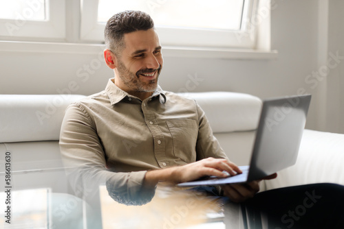 Confident happy middle aged businessman working on laptop, sitting on couch in modern office, free space