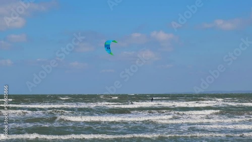 A man in a wetsuit on a parachute rides a board on the waves of the sea. A young man performs a trick in the air against the sky. Water sports, kitesurfing, paragliding, hydrofoil, surfing photo