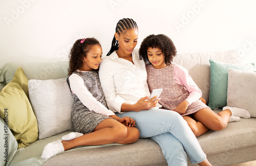 African American Mom And Two Daughters Using Phone At Home
