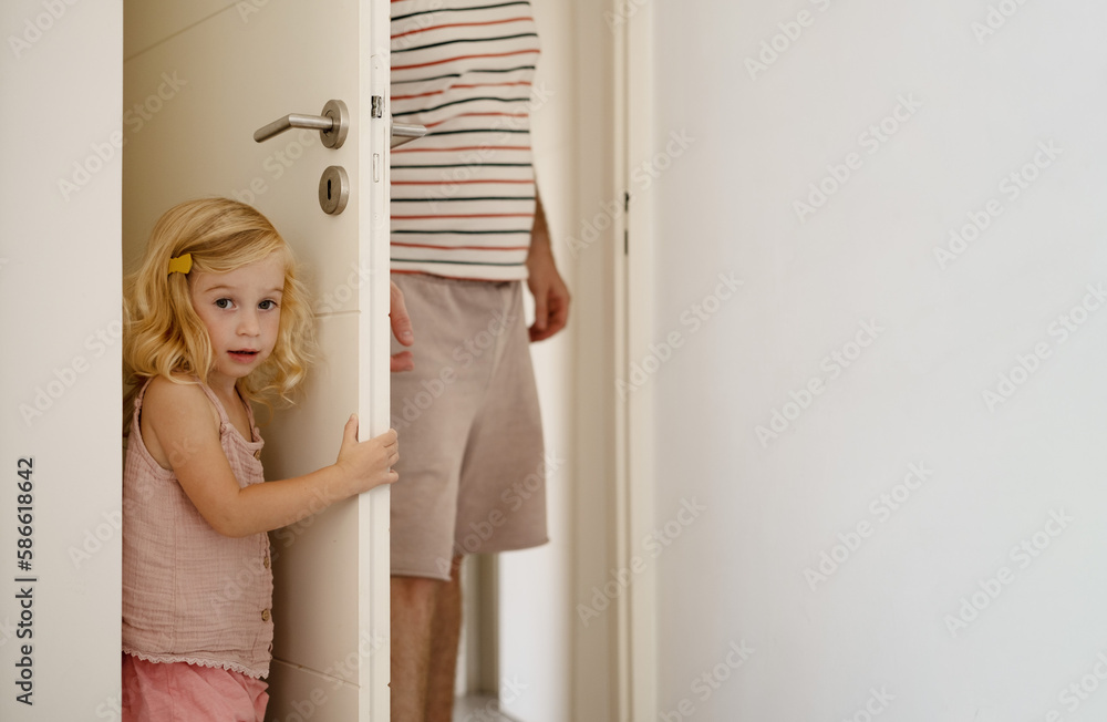 Man and girl playing hide-and-seek at home.Child hiding behind door from parent, playing together.Father spending leisure time with kid concept.Copy space. Man and girl playing hide-and-seek at home.Child hiding behind door from parent, playing together.Father spending leisure time with kid concept.Copy space.