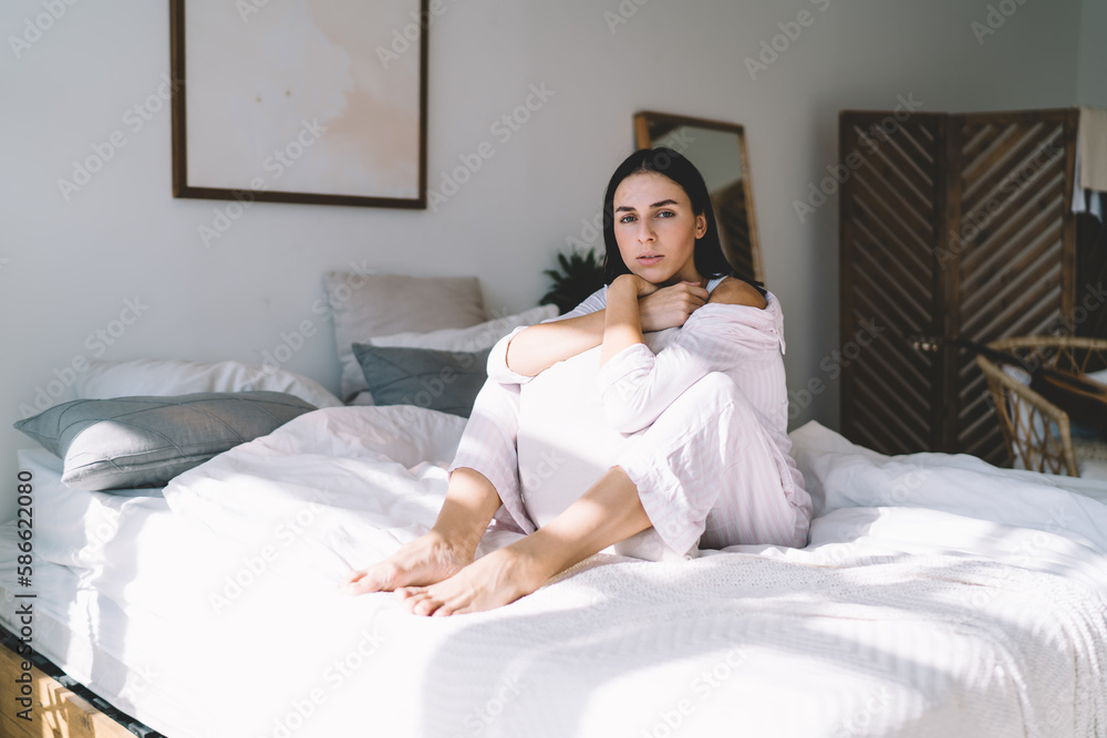 Thoughtful woman resting on bed hugging pillow