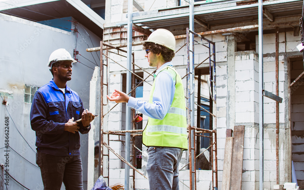 Two diversity male engineers team working, inspecting outdoor at construction site, wearing hard hats for safety, talking, discussing, planning for building. Career, Industry Concept. Two diversity male engineers team working, inspecting outdoor at construction site, wearing hard hats for safety, talking, discussing, planning for building. Career, Industry Concept.
