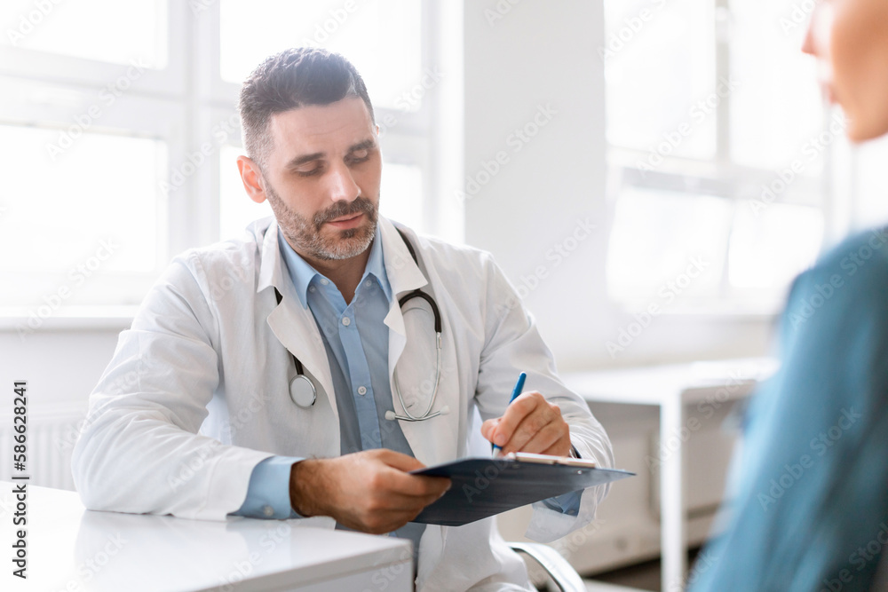 Doctor man listening female patient telling about health problems during consultation and noting personal information