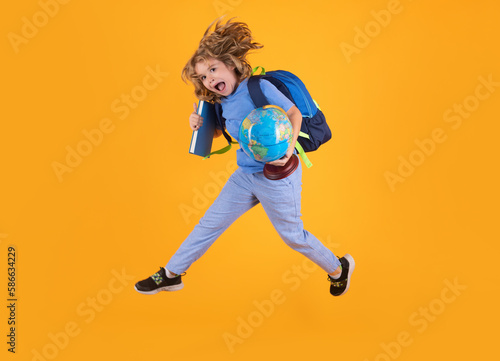 Shool kid jump with school bag and globe. Funny excited school concept. Little student boy with backpack go to study, jumping. Schoolchild, pupil jump on yellow isolated background.