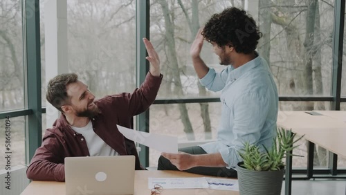 deadline, teamwork and success concept - creative multiethnic team of two employees with computer making high five at office