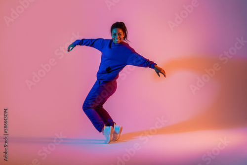 Street dance style. Happy black female hip-hop dancer dancing in neon pink lights, studio background, free space © Prostock-studio