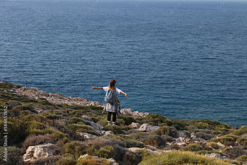 Back view of young woman hiking at the rocky coastline of atlantic ocean. Female hiker on the green hill washed by the sea. Traveling alone concept. Copy space, background. Back view of young woman hiking at the rocky coastline of atlantic ocean. Female hiker on the green hill washed by the sea. Traveling alone concept. Copy space, background.