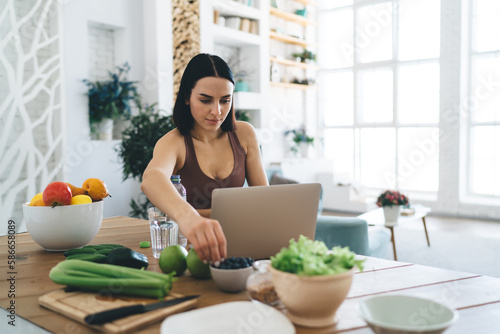 Focused woman watching video on laptop while preparing healthy meal
