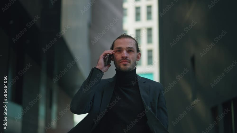Serious successful businessman enjoying mobile phone conversation while standing outdoors in evening city. Prosperous male entrepreneur calling via smartphone device. Connecting with technology
