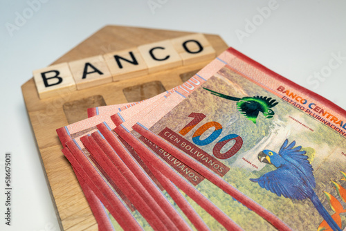 Bolivian money and the symbol of the bank of Colombia, a wooden miniature with the inscription banco, A lot of highest denomination banknotes, financial and business concept