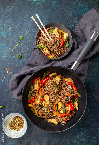 Japanese dish buckwheat soba noodles with chicken and vegetables carrot, bell pepper and green beans in wok on dark blue background