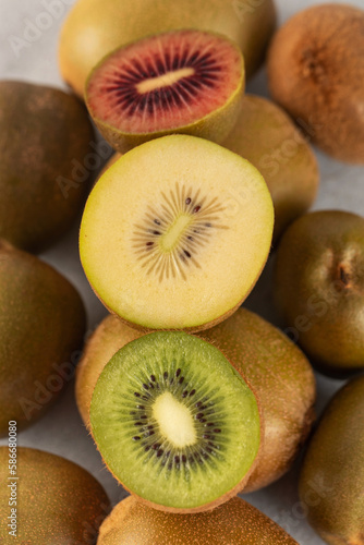 Different varieties of kiwi lie in a pile on the table. Halves of red, yellow and green kiwi. 