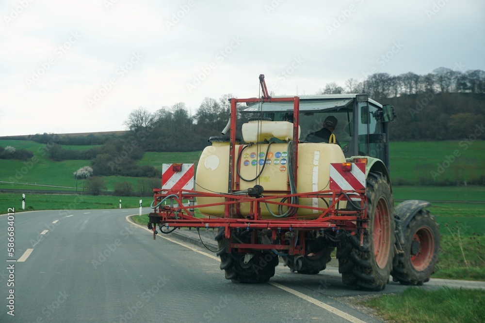 Alter Trecker mit Wassertank fährt von Straße auf Feldweg bei Regen am Mittag im Frühling Alter Trecker mit Wassertank fährt von Straße auf Feldweg bei Regen am Mittag im Frühling