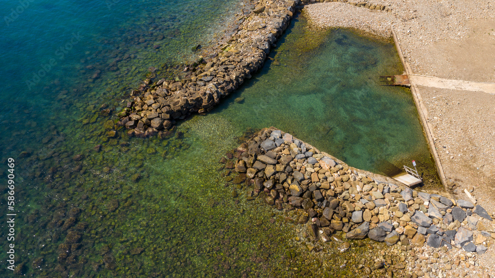 Aerial view of a long artificial reef near a small sandy cove near the sea. The beach is located in Santa Marinella, near Rome, Italy.