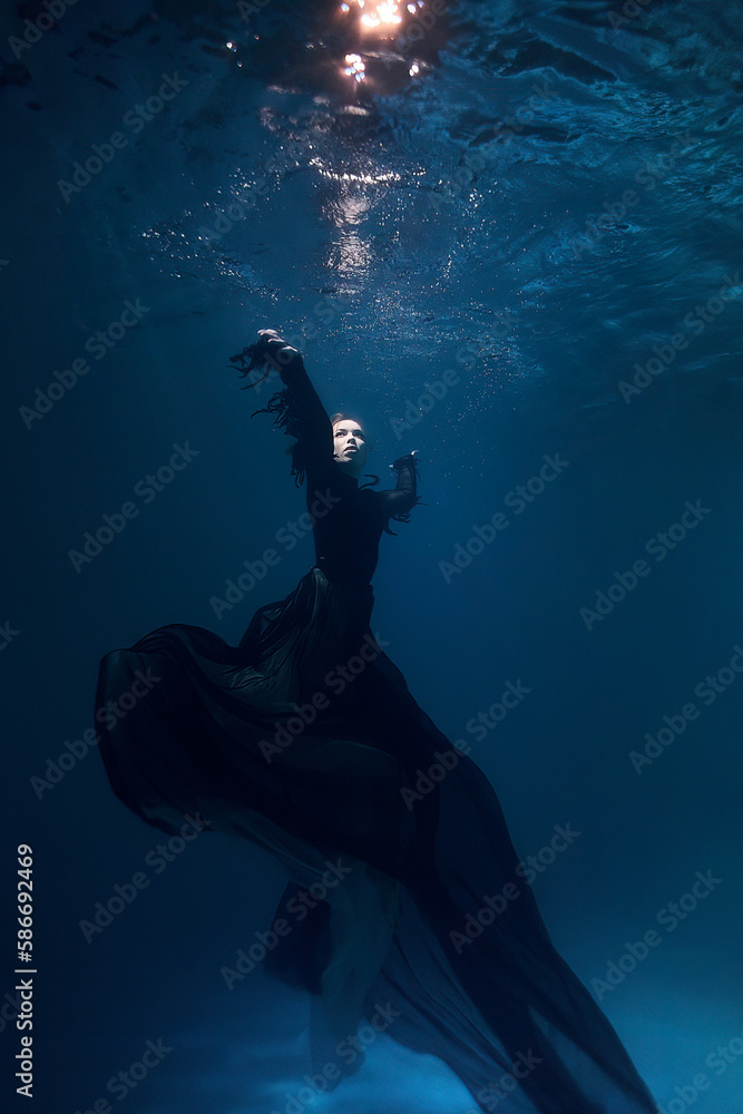 beautiful woman under water at a depth in a black witch dress. fantasy fairy tale