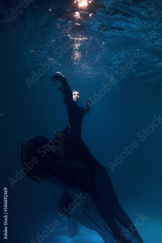 beautiful woman under water at a depth in a black witch dress. fantasy fairy tale